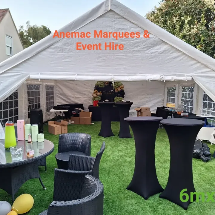 An open garden marquee with black-covered poseur tables, black wicker seating and a balloon display at the rear