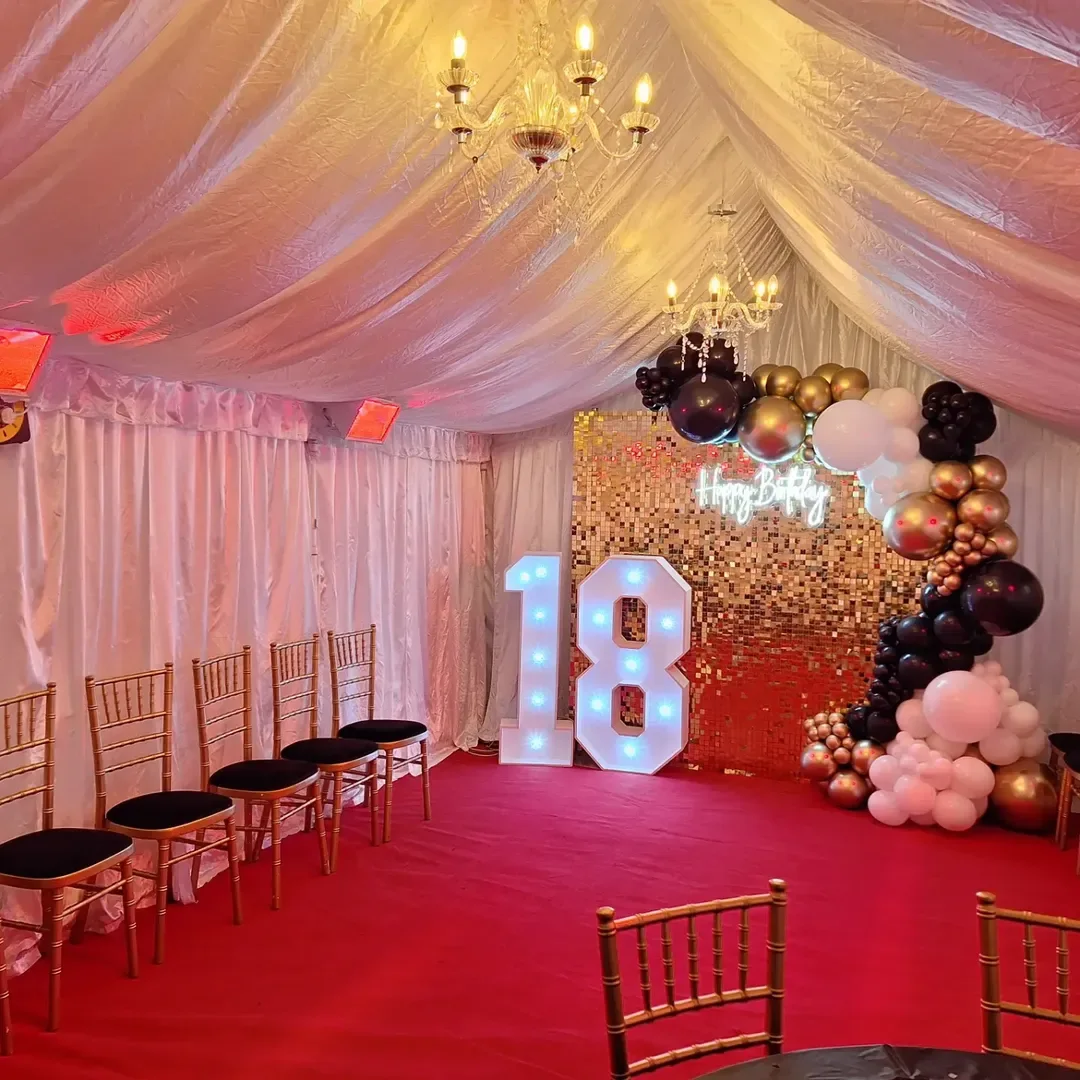 Marquee interior with gold, black and white balloons, an illuminated 18 and chandeliers