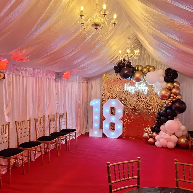 Marquee interior with gold, black and white balloons, an illuminated 18 and chandeliers