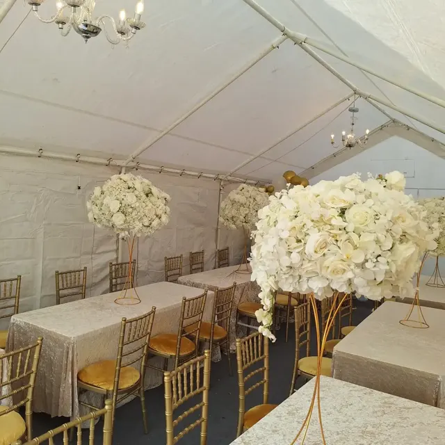 Dining tables with tall white floral centrepieces and gold Chiavari chairs under chandeliers