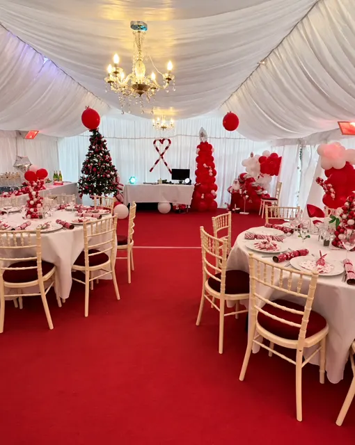Festive marquee interior with white drapes, chandeliers, red carpet and a Christmas tree