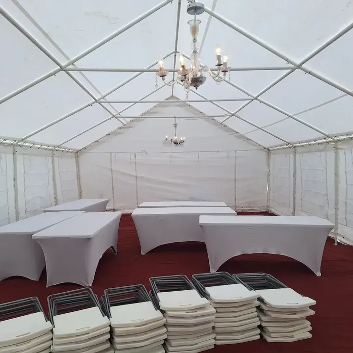 A prepared marquee interior with white-clothed tables, stacked chairs and hanging chandeliers