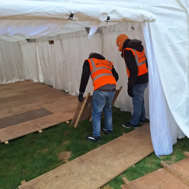 Two team members laying wooden flooring boards inside a marquee during setup