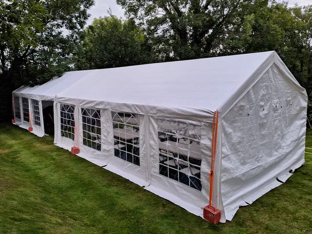 A white window-sided marquee on a lawn beside trees