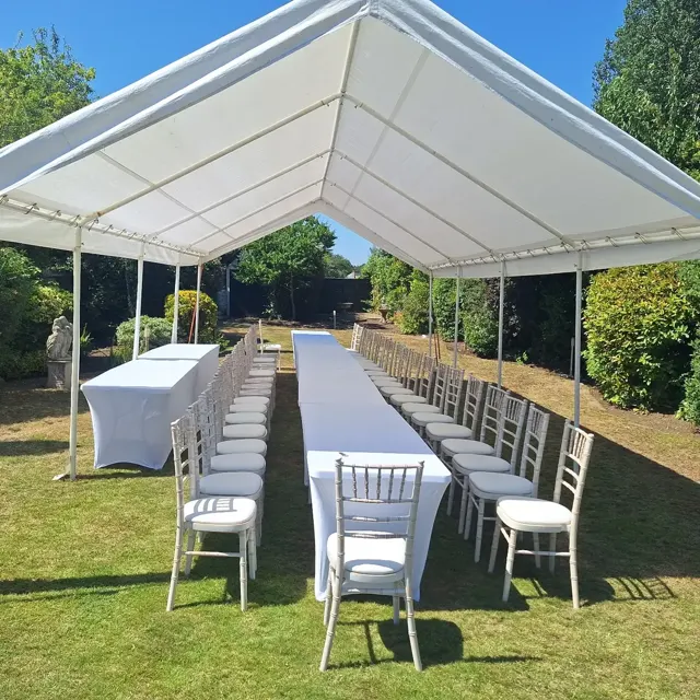 Open-sided garden marquee with long white-clothed tables and white Chiavari chairs