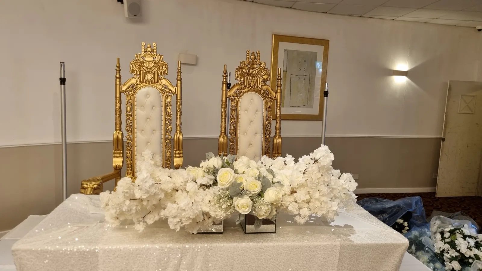 A pair of white and gold throne chairs behind a floral top table