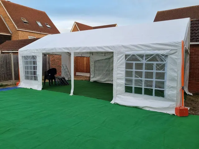 An open-fronted marquee beside a house with green flooring